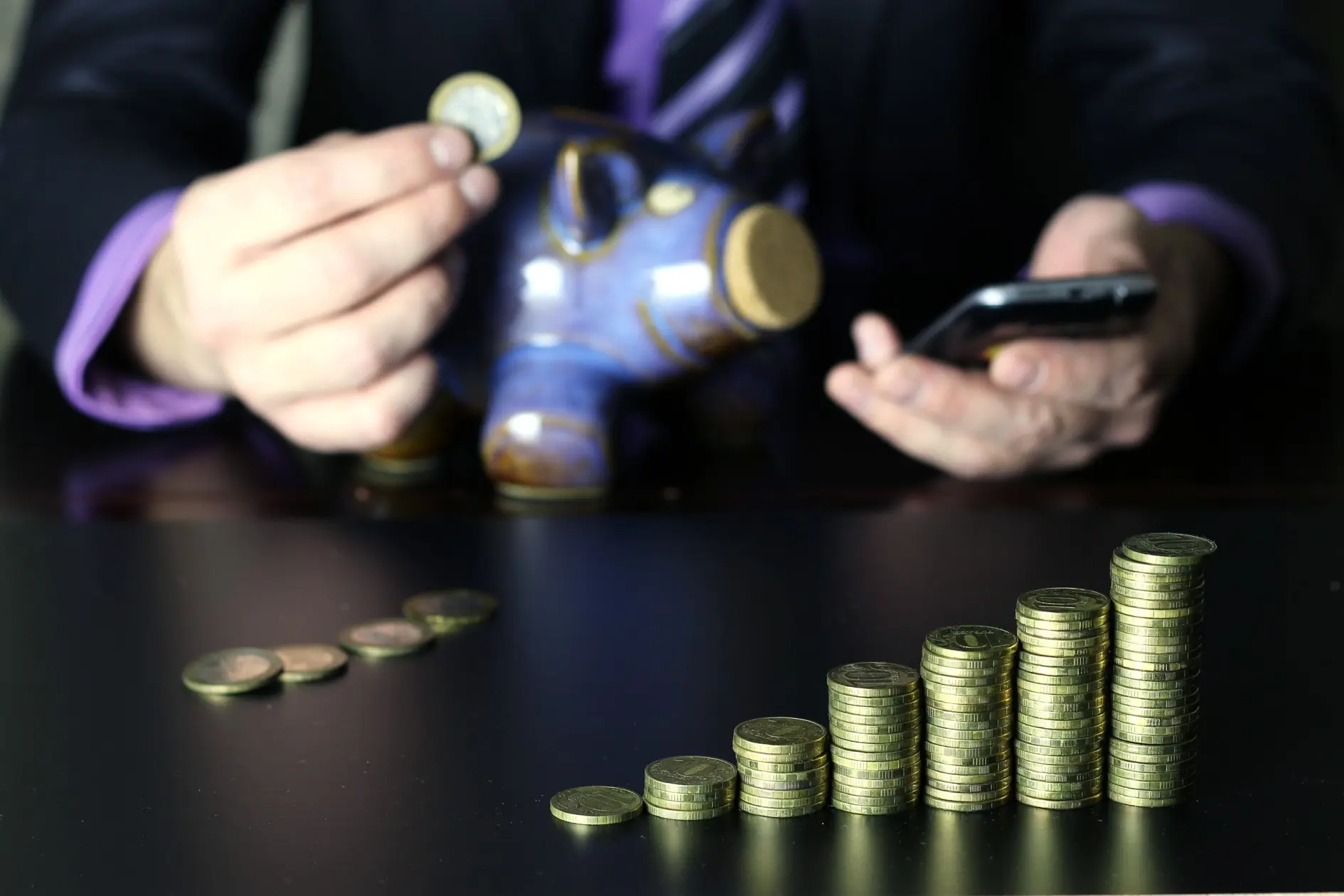 Business professional holding a piggy bank and phone beside growing coin stacks, representing hidden telecom cost savings uncovered through Microsoft Dynamics 365 and legacy system modernization